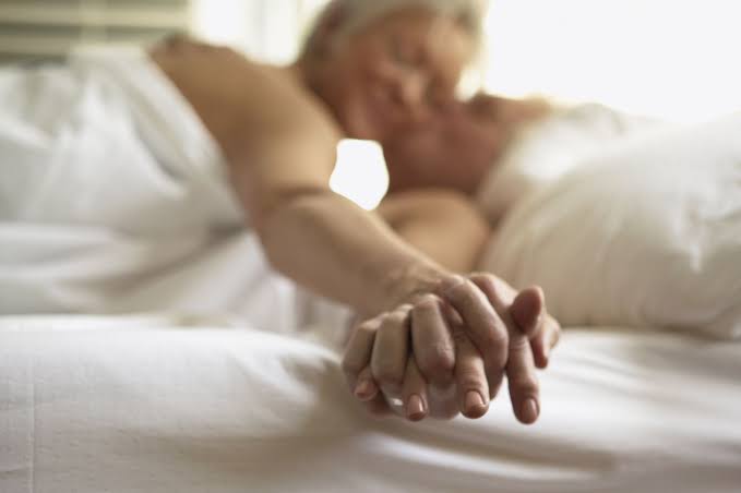 Couple holding hands intimately in bed representing connection and wellness